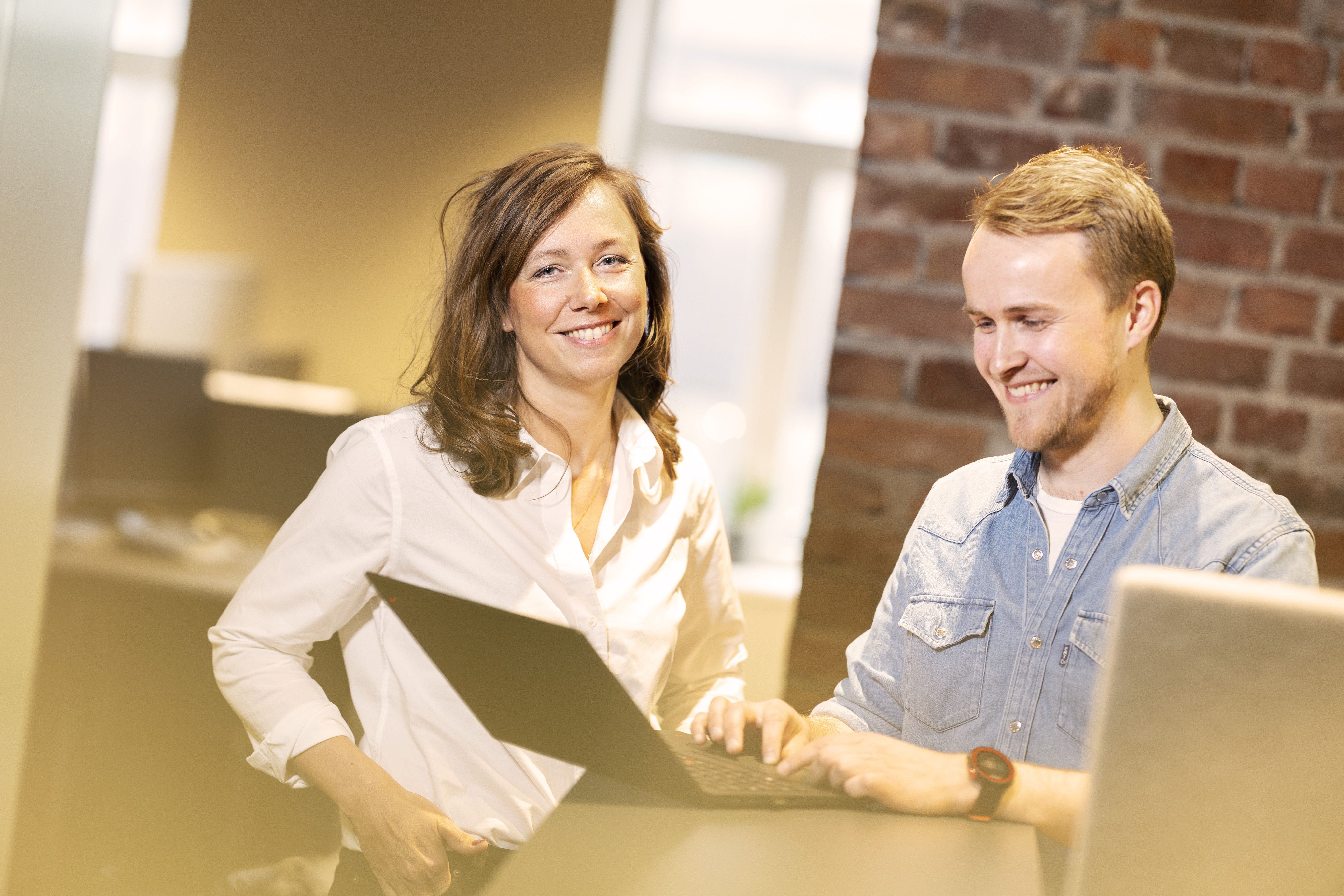 En mann og en dame sitter ved en PC og smiler